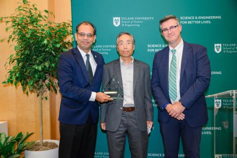 Three men in suits pose for a photograph with a glass award.