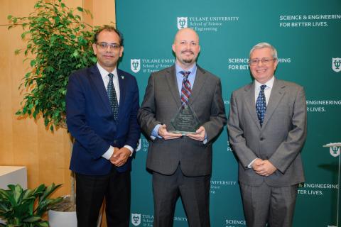 Three men in suits pose for a photo, two hold awards.