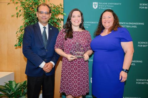 Three people stand for an award photo, two men and one woman in the center holding an award.