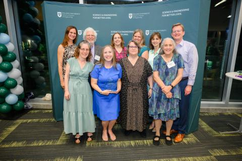 A group of ten people pose for a photo in front of a green backdrop.