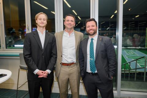 Three men in suits pose for a photograph indoors.