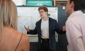 Young man in suit explains poster to two people.