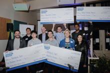 Winners hold giant checks at an awards ceremony.