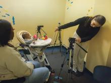 Woman filming baby in high chair with cameras and tripods.