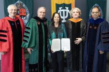 Five academics in regalia stand together, holding a document.