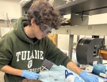 Student in goggles and gloves works at a lab bench.