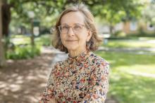 Woman with glasses and floral shirt outdoors.